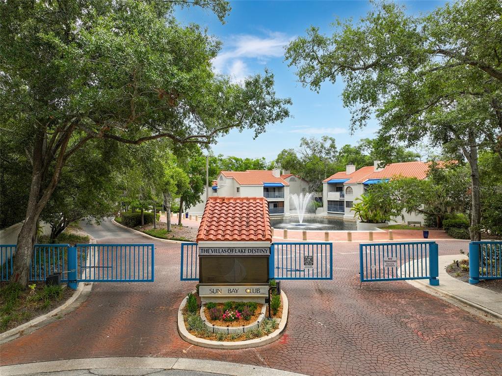 A gated entrance with a fountain and multi-story apartment buildings in a landscaped setting — 1000 WINDERLEY PLACE UNIT 141, MAITLAND, FL