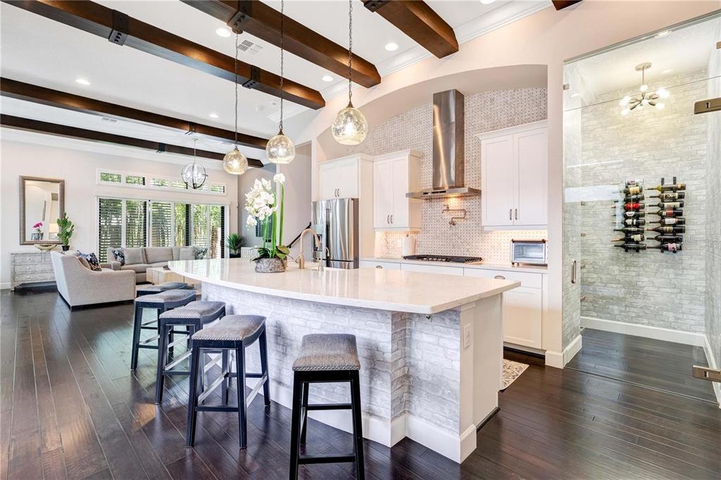 A kitchen with a white island, dark wood floors, exposed ceiling beams, and a glass-enclosed wine cellar — 8449 VIA VITTORIA WAY, ORLANDO, FL