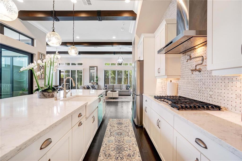 A modern kitchen features white cabinetry, quartz countertops, a farmhouse sink, and dark wood flooring — 8449 VIA VITTORIA WAY, ORLANDO, FL