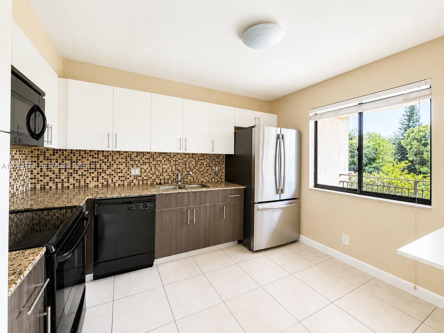 A kitchen features white upper cabinets, wood-tone lower cabinets, granite countertops, and stainless steel appliances — 405 LAKEVIEW DR # 202, Weston FL 33326, WESTON, FL