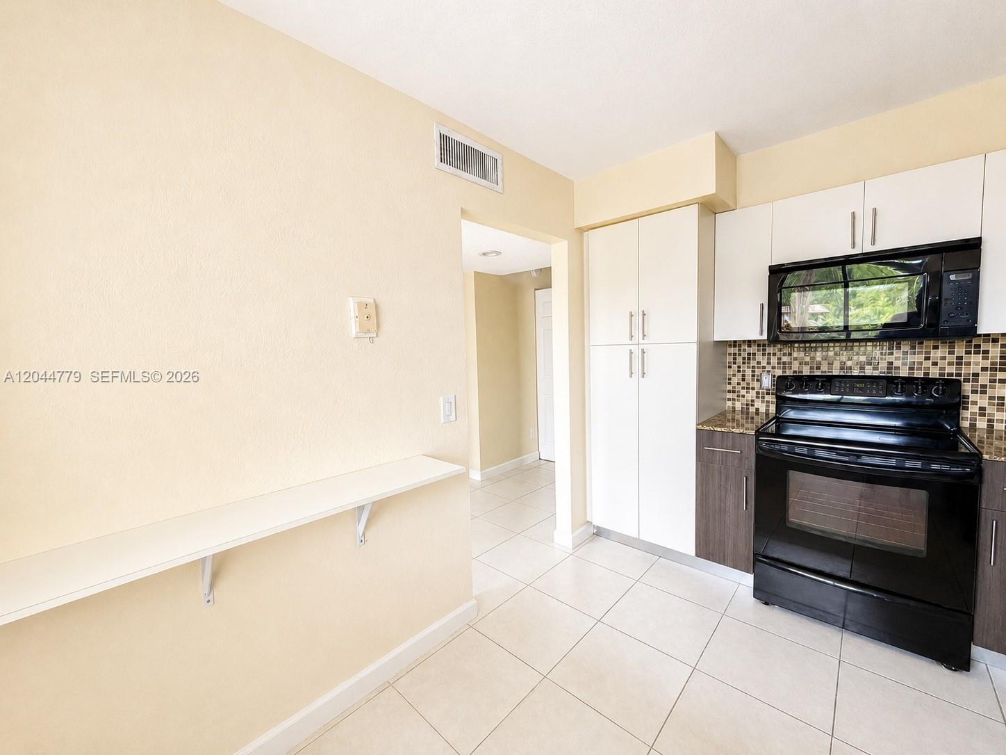 A kitchen features white and dark wood cabinetry, a black stove, and a wall-mounted shelf — 405 LAKEVIEW DR # 202, Weston FL 33326, WESTON, FL