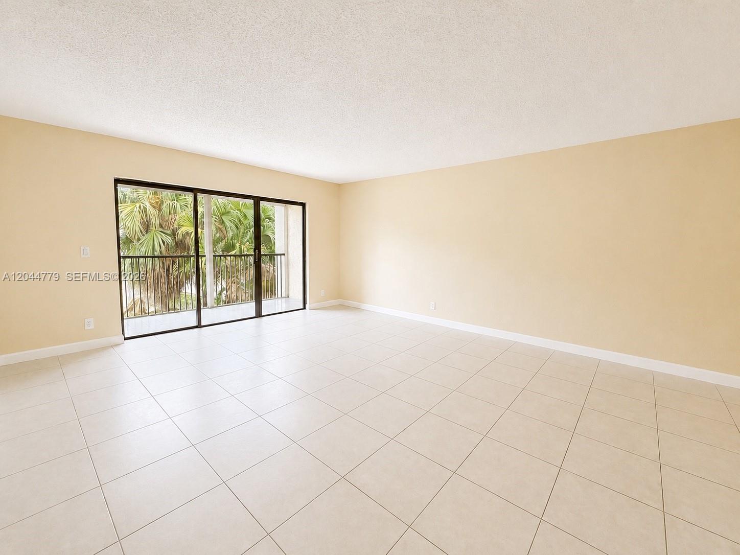 An empty room features beige walls, light-colored tile flooring, and a sliding glass door balcony — 405 LAKEVIEW DR # 202, Weston FL 33326, WESTON, FL