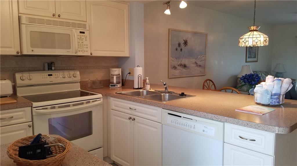 A kitchen features white cabinets, a white stove, a dishwasher, and a breakfast bar counter — 25275 RAMPART BOULEVARD UNIT 1608, PUNTA GORDA, FL