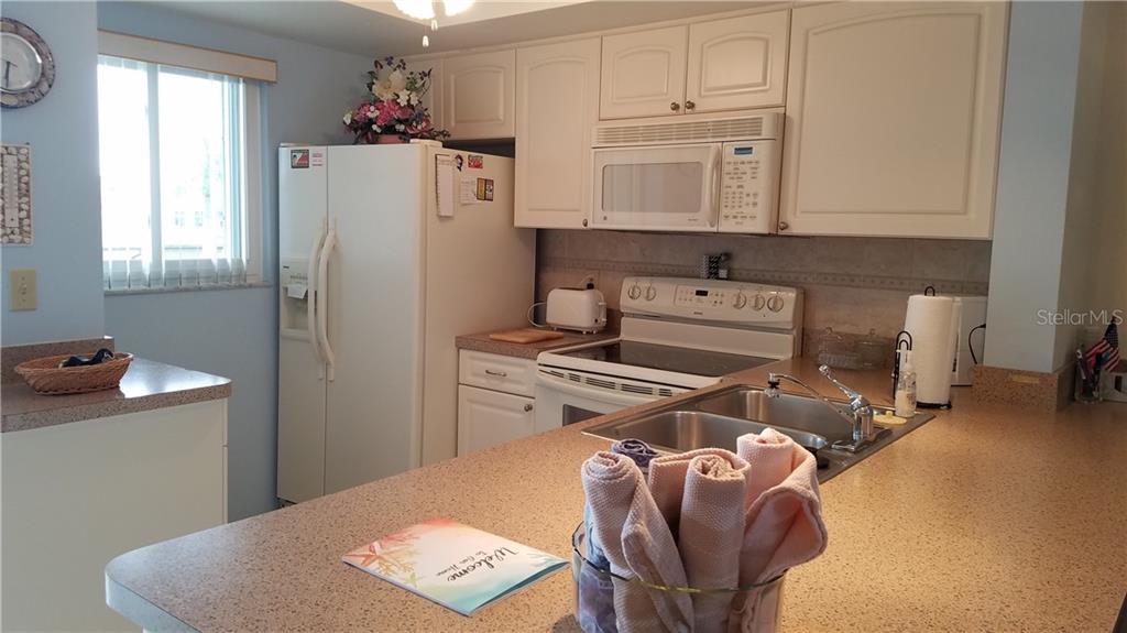 A kitchen features white cabinets, a white refrigerator, a microwave, and a speckled countertop — 25275 RAMPART BOULEVARD UNIT 1608, PUNTA GORDA, FL