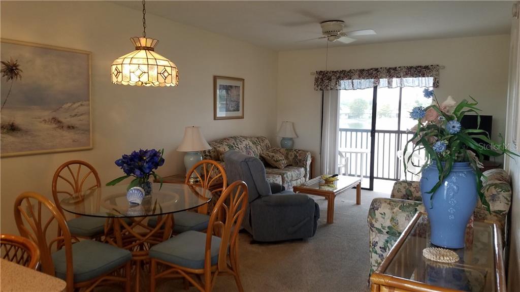 A living and dining area features a glass table, floral furniture, and a sliding glass door — 25275 RAMPART BOULEVARD UNIT 1608, PUNTA GORDA, FL