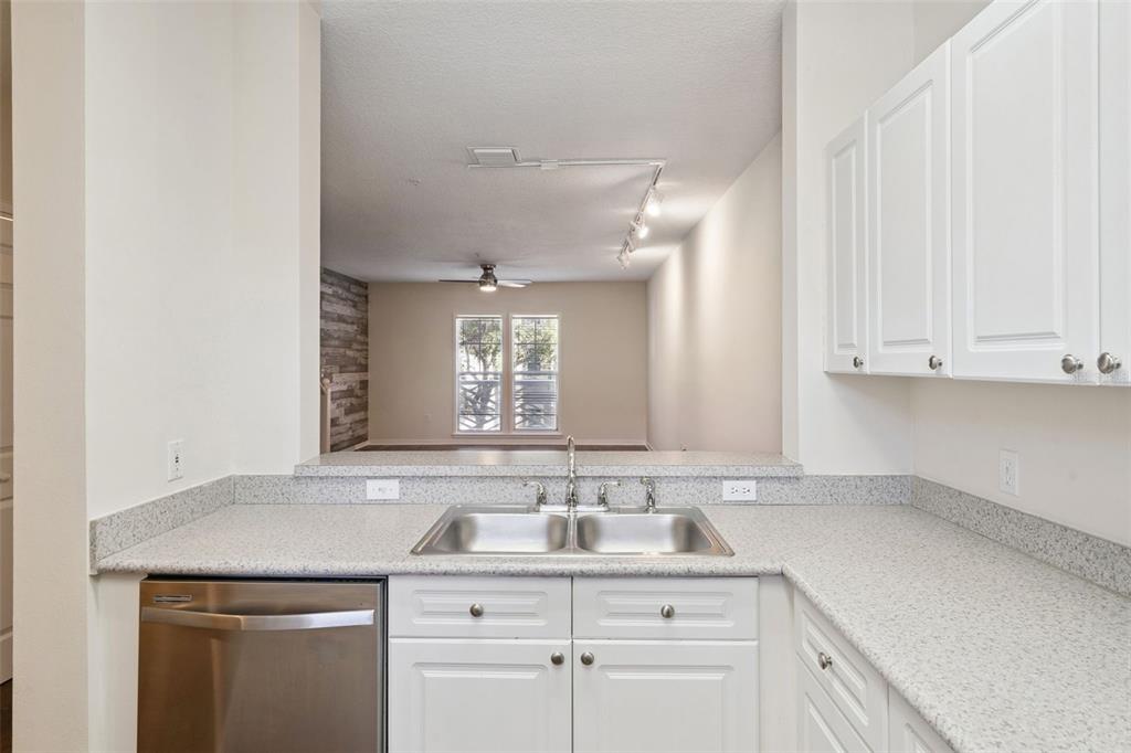 A kitchen with white cabinets, speckled countertops, and a stainless steel sink overlooking a living area — 720 CELEBRATION AVENUE UNIT 235, CELEBRATION, FL