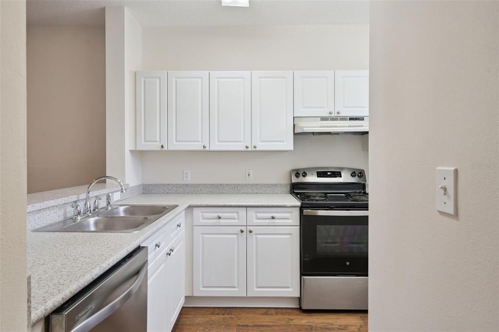 A kitchen features white cabinets, speckled countertops, stainless steel appliances, and wood-look flooring — 720 CELEBRATION AVENUE UNIT 235, CELEBRATION, FL