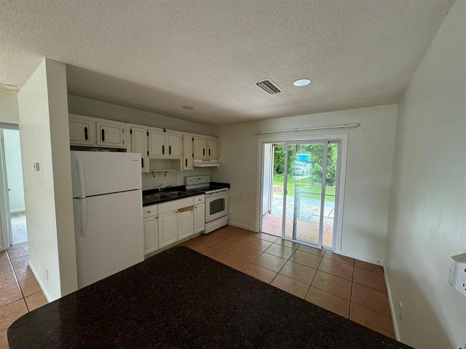 A kitchen with white cabinets, dark countertops, white appliances, and a sliding glass door — 3002 SE Camino Avenue, Stuart FL 34997, STUART, FL