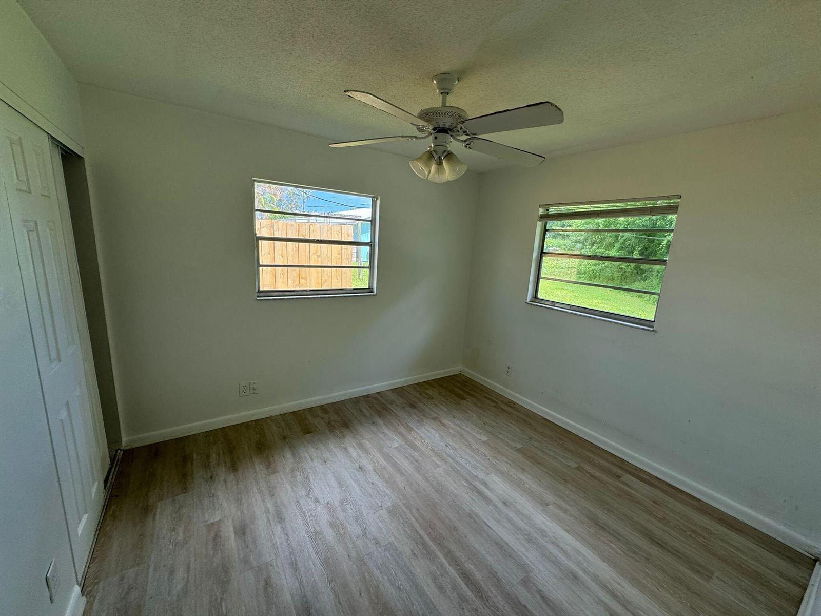 An empty bedroom with white walls, light wood-look flooring, a ceiling fan, and two windows — 3002 SE Camino Avenue, Stuart FL 34997, STUART, FL