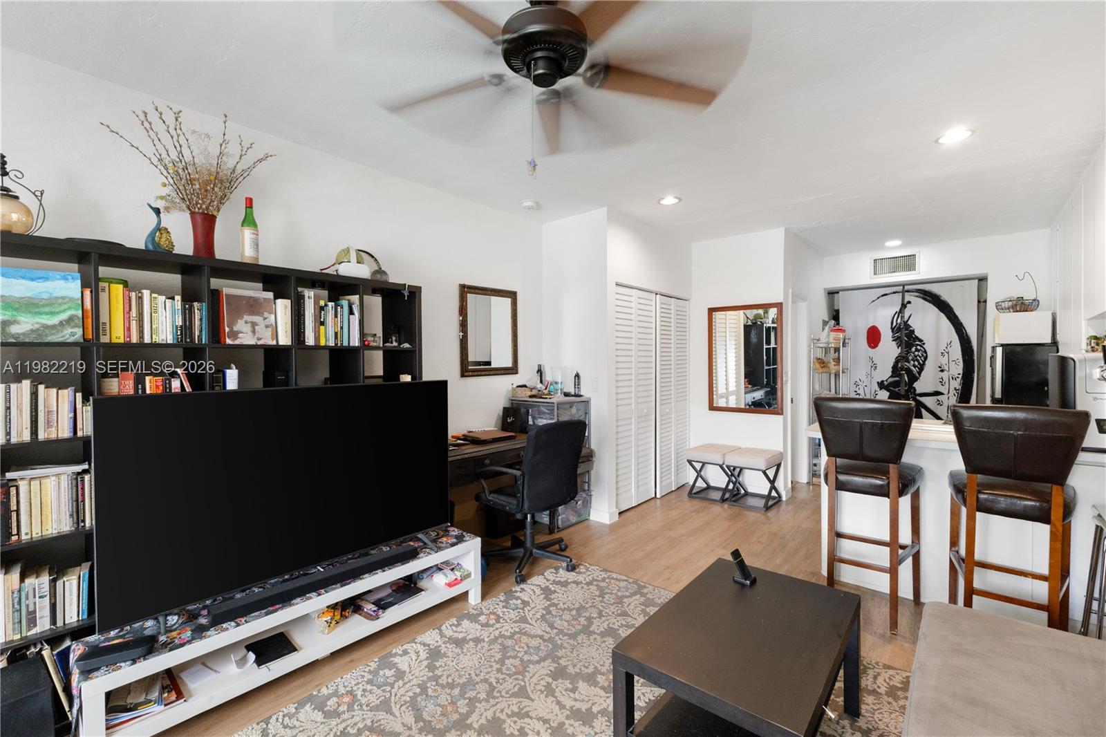 A living room features a large television, a bookshelf, a desk, and a breakfast bar — 2445 Lake Pancoast Dr # J, Miami Beach FL 33140, MIAMI BEACH, FL