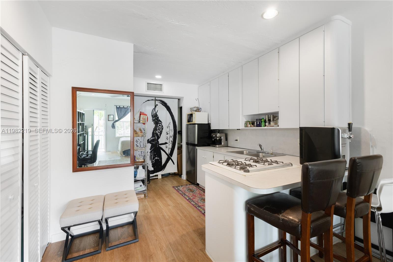 A small kitchen features white cabinets, a gas cooktop, and a breakfast bar with stools — 2445 Lake Pancoast Dr # J, Miami Beach FL 33140, MIAMI BEACH, FL