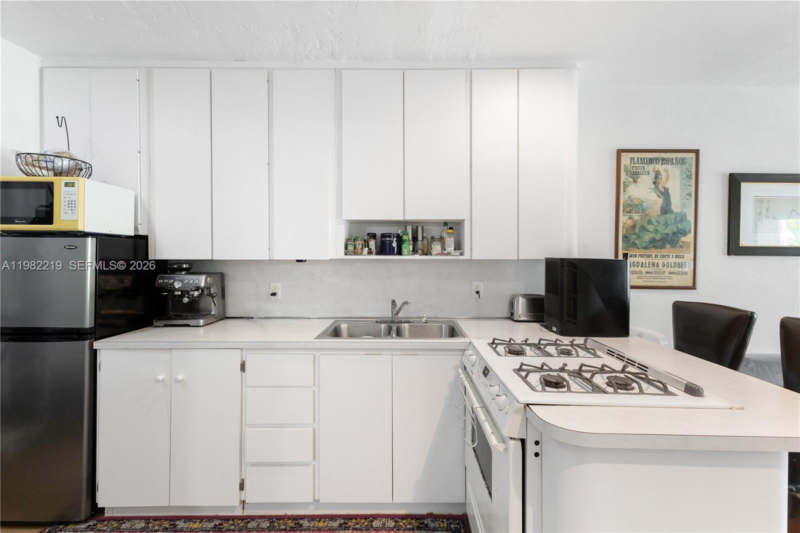 A kitchen features white cabinets, a gas stove, a stainless steel sink, and a refrigerator — 2445 Lake Pancoast Dr # J, Miami Beach FL 33140, MIAMI BEACH, FL