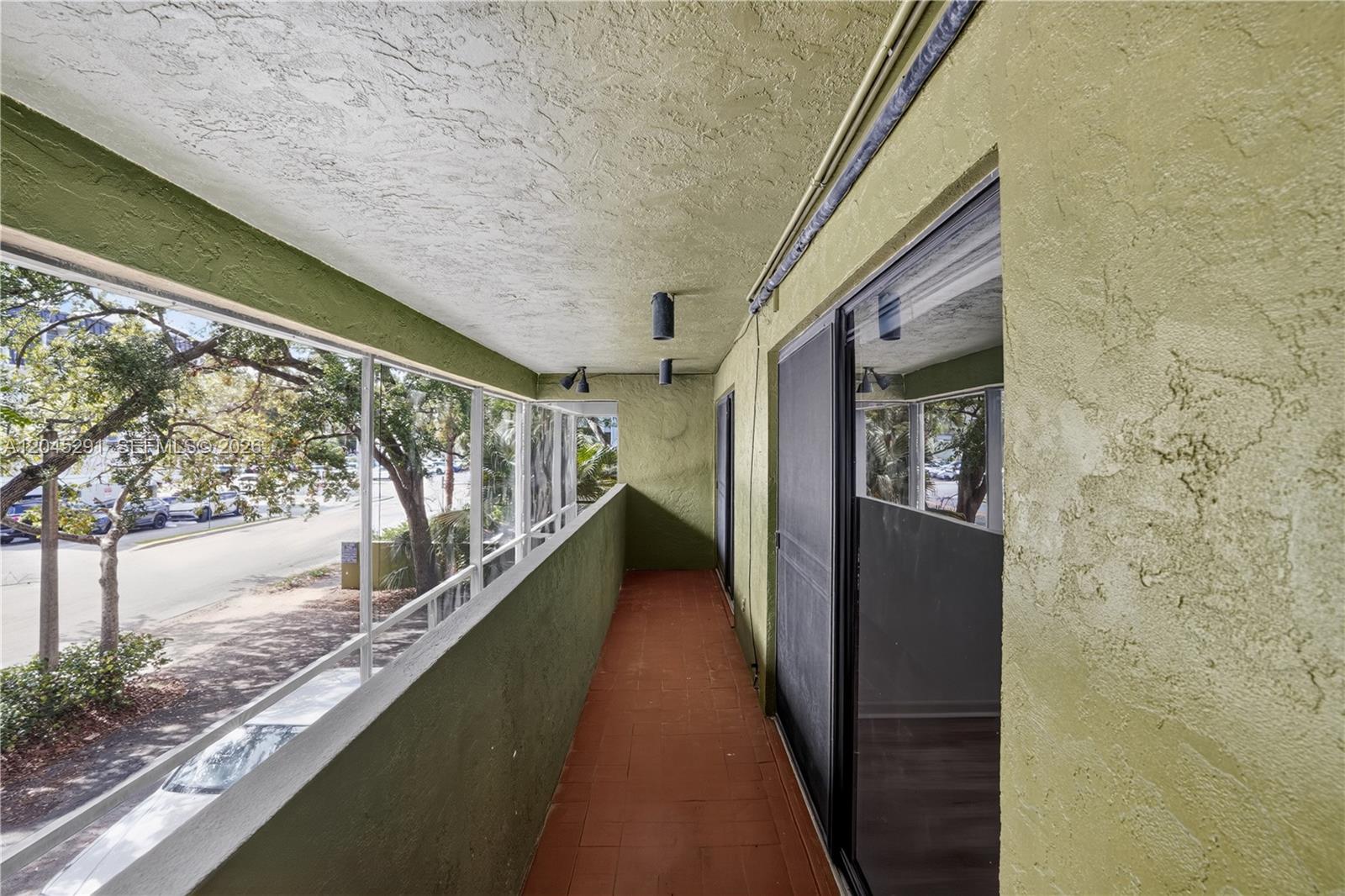 A covered balcony features green stucco walls, a red tiled floor, and large glass windows — 7420 SW 59th Ave # D, South Miami FL 33143, SOUTH MIAMI, FL
