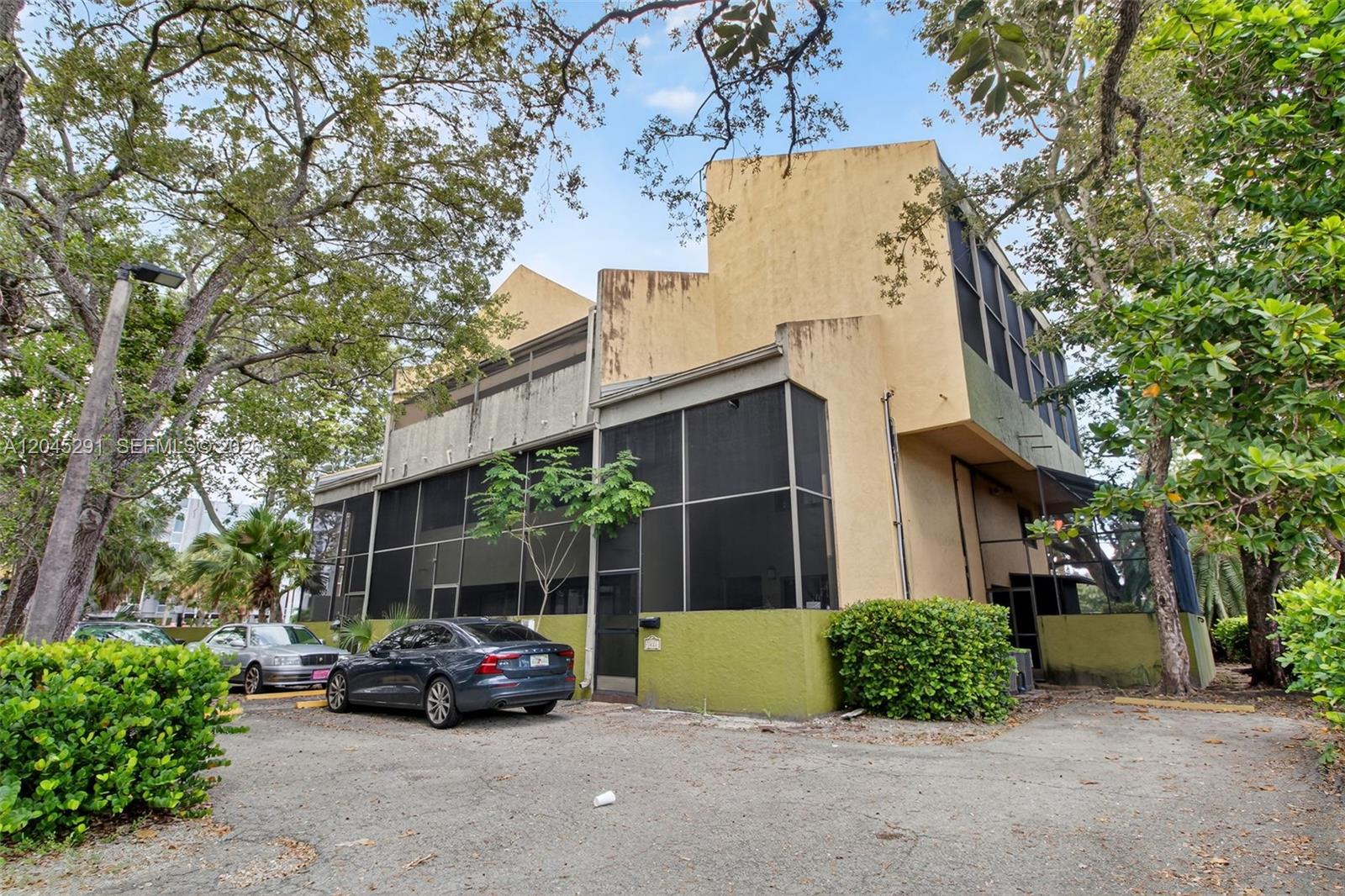 A two-story building with a screened-in porch and parking lot sits among mature trees — 7420 SW 59th Ave # D, South Miami FL 33143, SOUTH MIAMI, FL