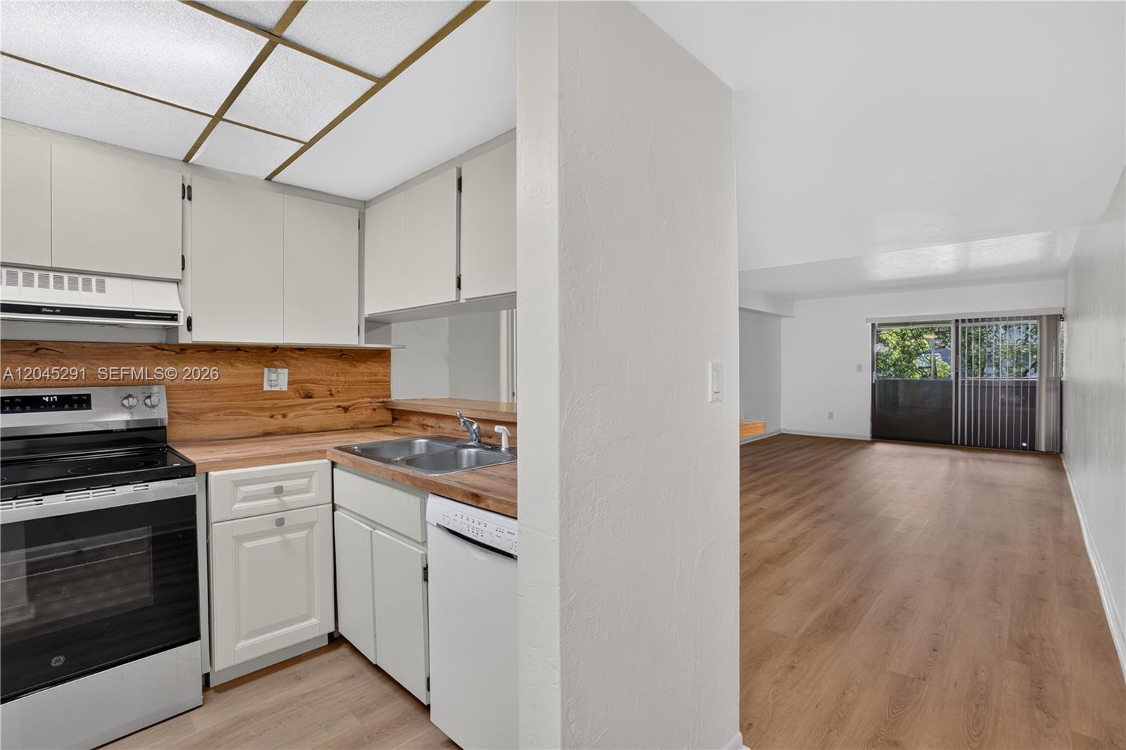 A kitchen with white cabinets and wood countertops opens into a living area with flooring — 7420 SW 59th Ave # D, South Miami FL 33143, SOUTH MIAMI, FL