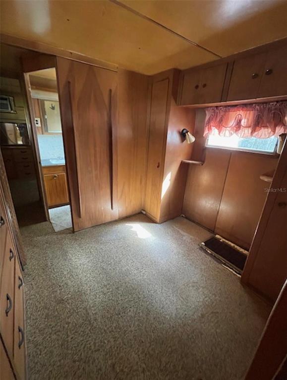 A small room with wood-paneled walls, built-in storage, a window with curtains, and carpeted flooring — 9736 WARRICK STREET, PORT RICHEY, FL