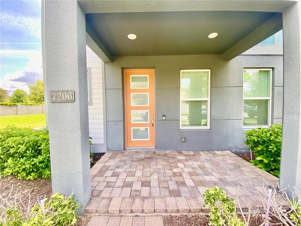 The front entrance features a paved porch, a light orange door, and gray exterior walls — 7206 CARRICKBEND LANE, ORLANDO, FL