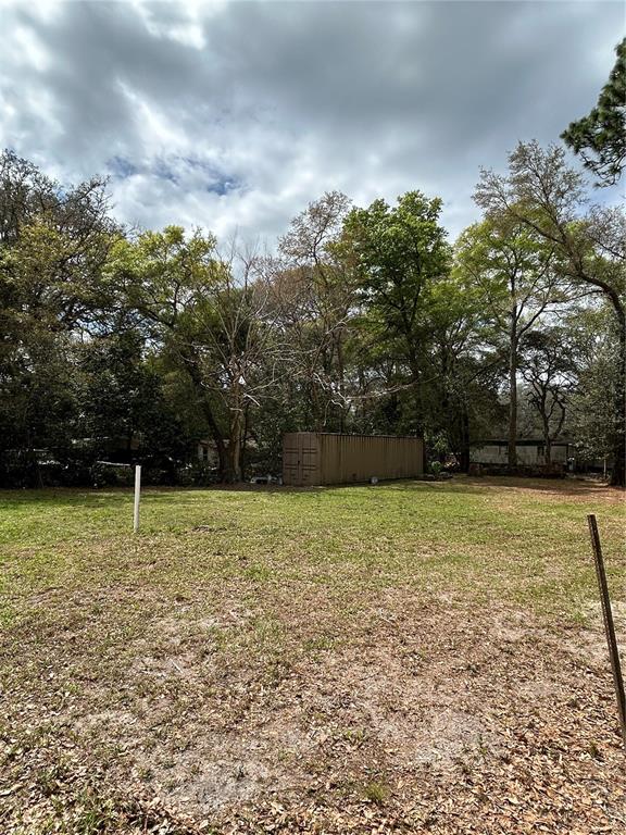 A grassy lot features a large metal storage container surrounded by mature trees — 4TH STREET, ALTOONA, FL