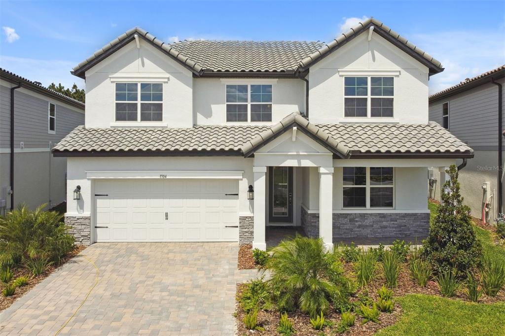A two-story house with a white stucco exterior, stone accents, and a paved driveway — 1704 SUTTONSET TRAIL, ZEPHYRHILLS, FL
