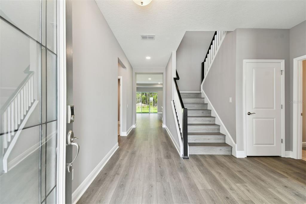 An entryway features light gray walls, wood-look flooring, and a staircase with a dark handrail — 1704 SUTTONSET TRAIL, ZEPHYRHILLS, FL