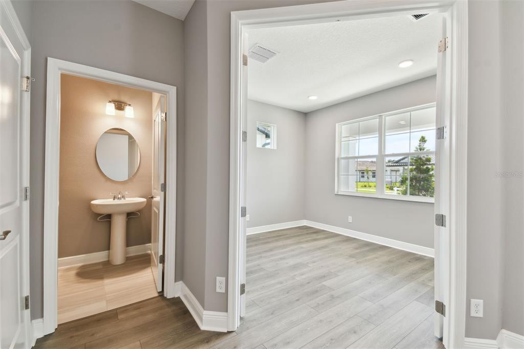 A view of a room with gray wood-look flooring and an adjacent half bathroom — 1704 SUTTONSET TRAIL, ZEPHYRHILLS, FL