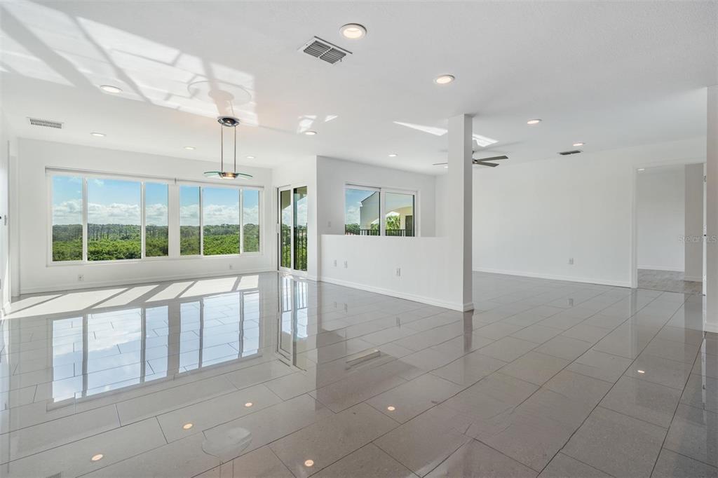 A spacious, bright room with white walls, glossy tile floors, and large windows overlooking trees — 244 MARINER DRIVE UNIT 244, TARPON SPRINGS, FL