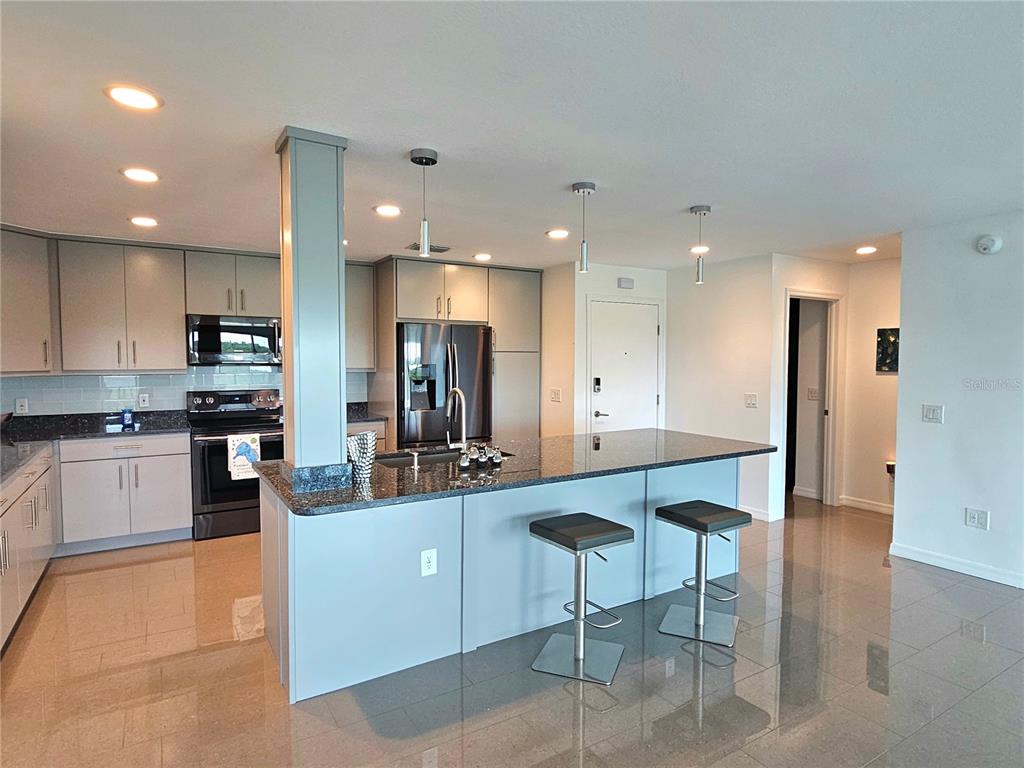 A modern kitchen features gray cabinetry, granite countertops, a central island, and tile flooring — 244 MARINER DRIVE UNIT 244, TARPON SPRINGS, FL