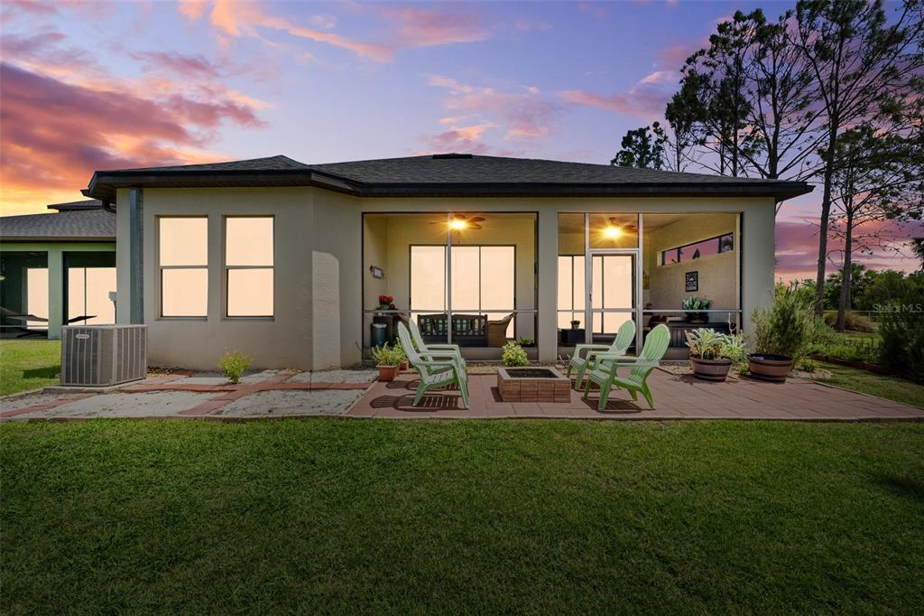 A rear view of a house with a screened-in patio, fire pit, and green lawn — 4501 ROLLING GREEN DRIVE, WESLEY CHAPEL, FL