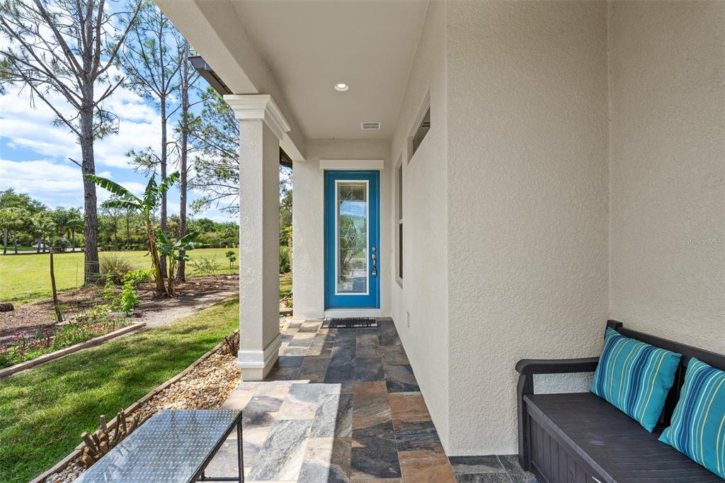 A covered porch features stone tile flooring, a blue front door, and a black bench — 4501 ROLLING GREEN DRIVE, WESLEY CHAPEL, FL