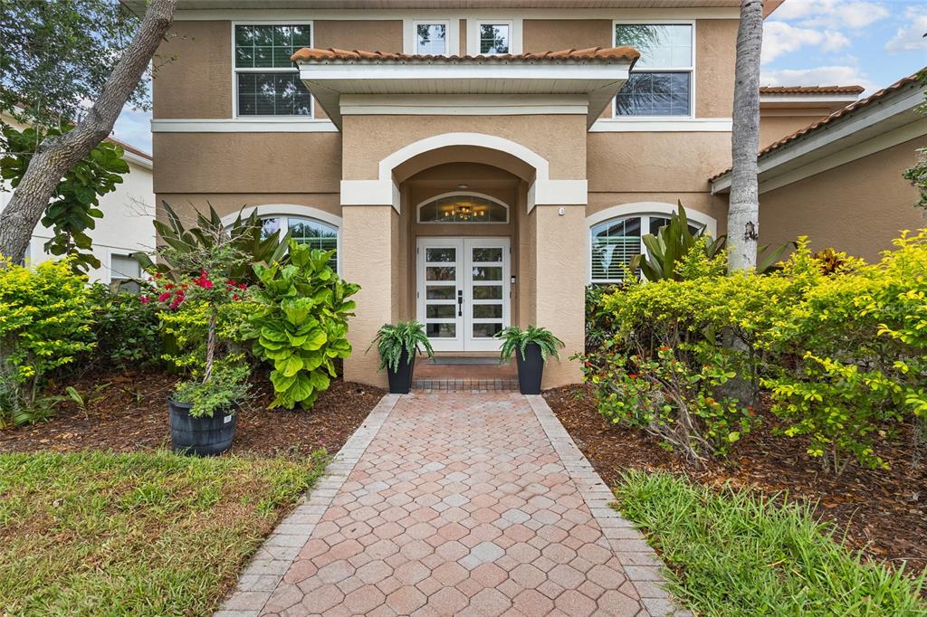 A paved walkway leads to the double front doors of a tan two-story stucco house — 7627 DESERT INN WAY, BRADENTON, FL