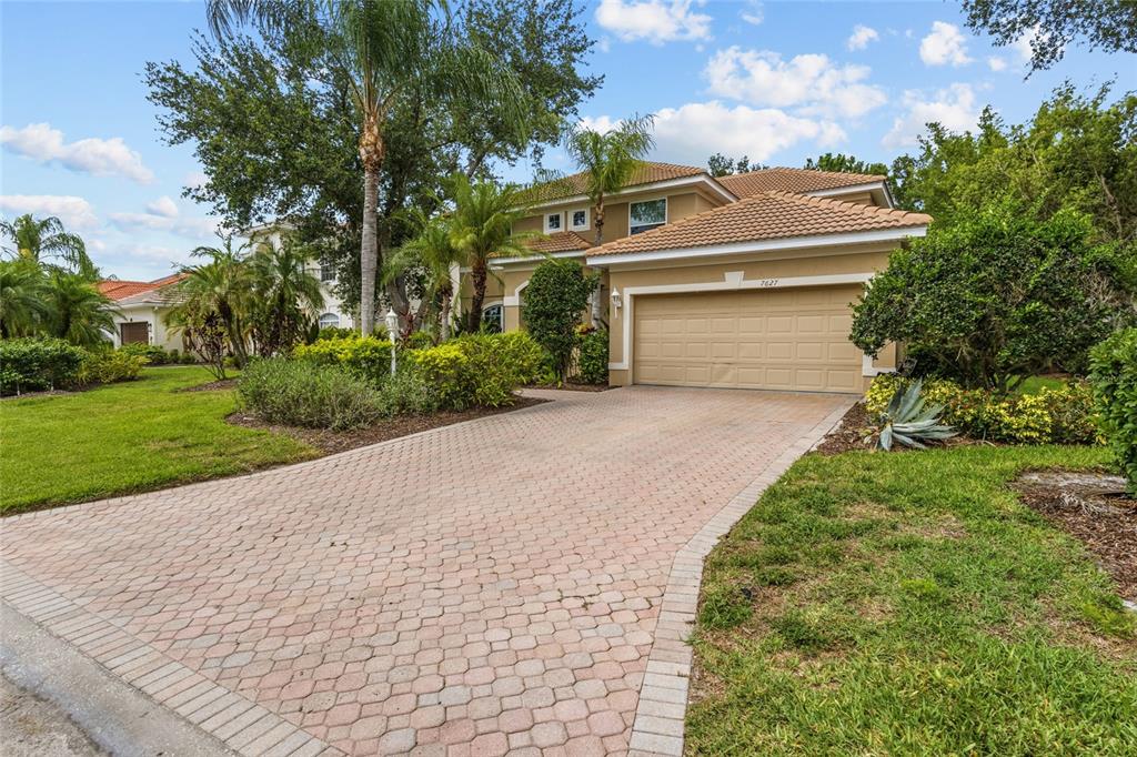 A two-story house with a tan stucco exterior, a tile roof, and a paved driveway — 7627 DESERT INN WAY, BRADENTON, FL