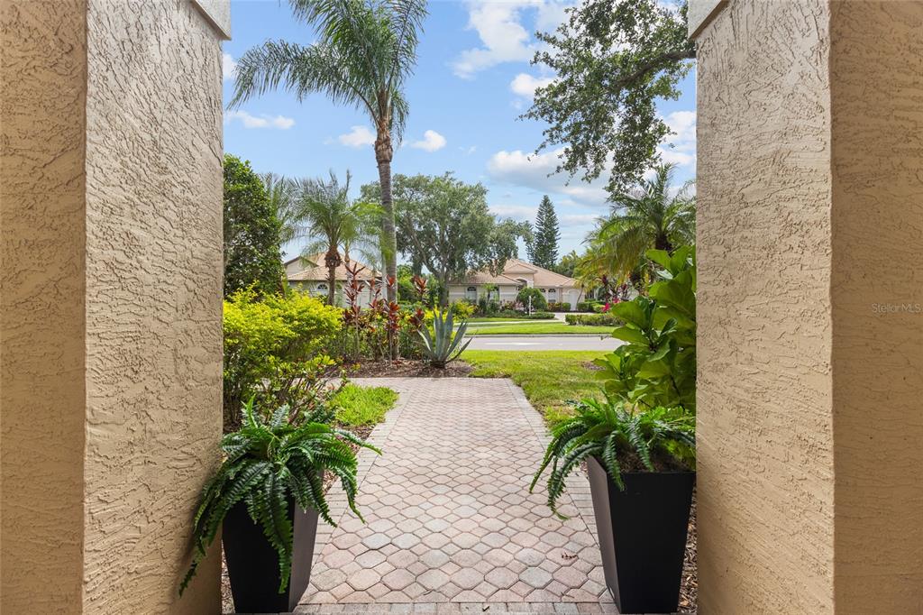 A paved walkway leads from a covered entryway toward a suburban street with palm trees — 7627 DESERT INN WAY, BRADENTON, FL