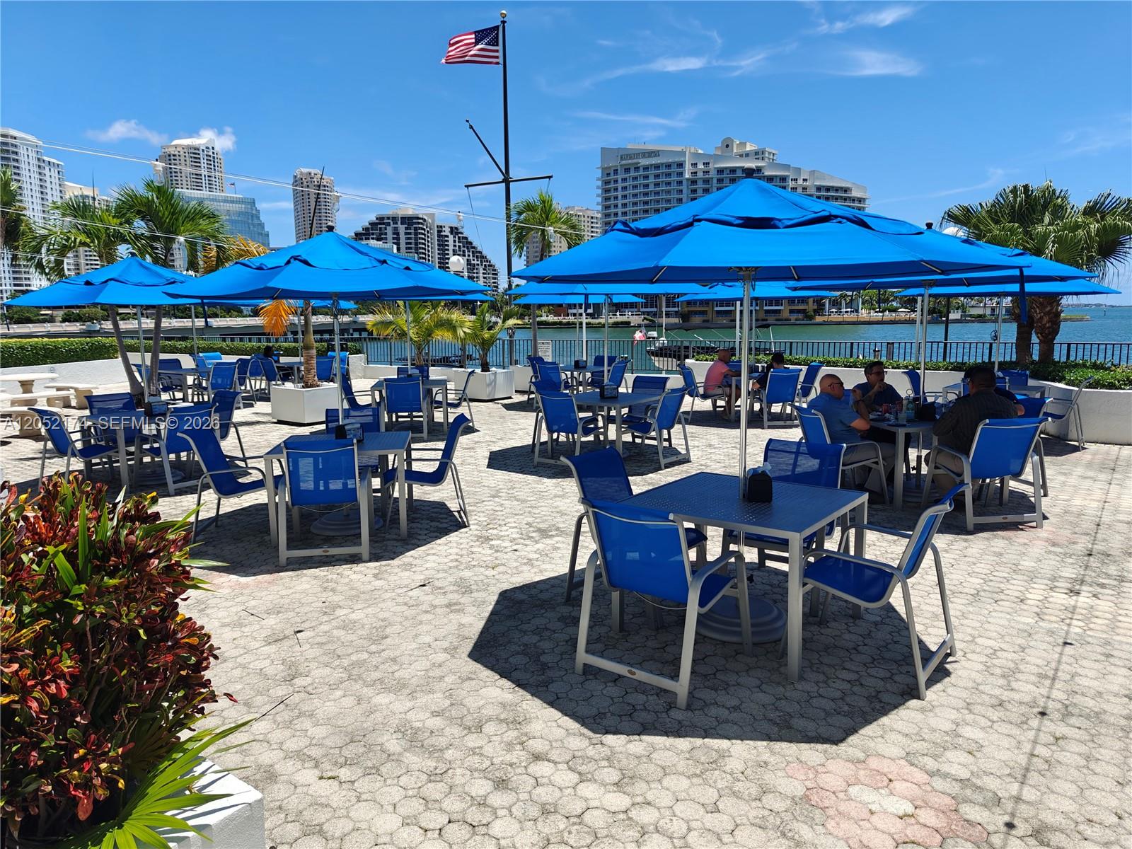An outdoor patio features blue umbrellas, tables, and chairs overlooking a waterfront city view — 999 Brickell Bay Dr # 1904, Miami FL 33131, MIAMI, FL
