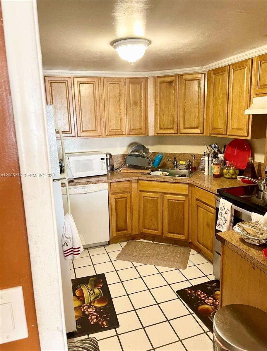 A kitchen features wooden cabinets, a white dishwasher, a corner sink, and tiled flooring — 3301 Spanish Moss Ter # 510, Lauderhill FL 33319, LAUDERHILL, FL