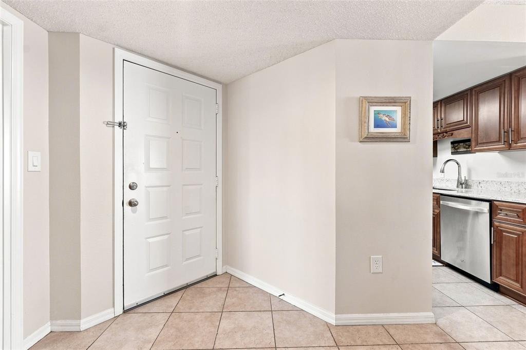An entryway with a white door and tiled floor leads into a kitchen with cabinets — 3601 S BANANA RIVER BOULEVARD UNIT A304, COCOA BEACH, FL