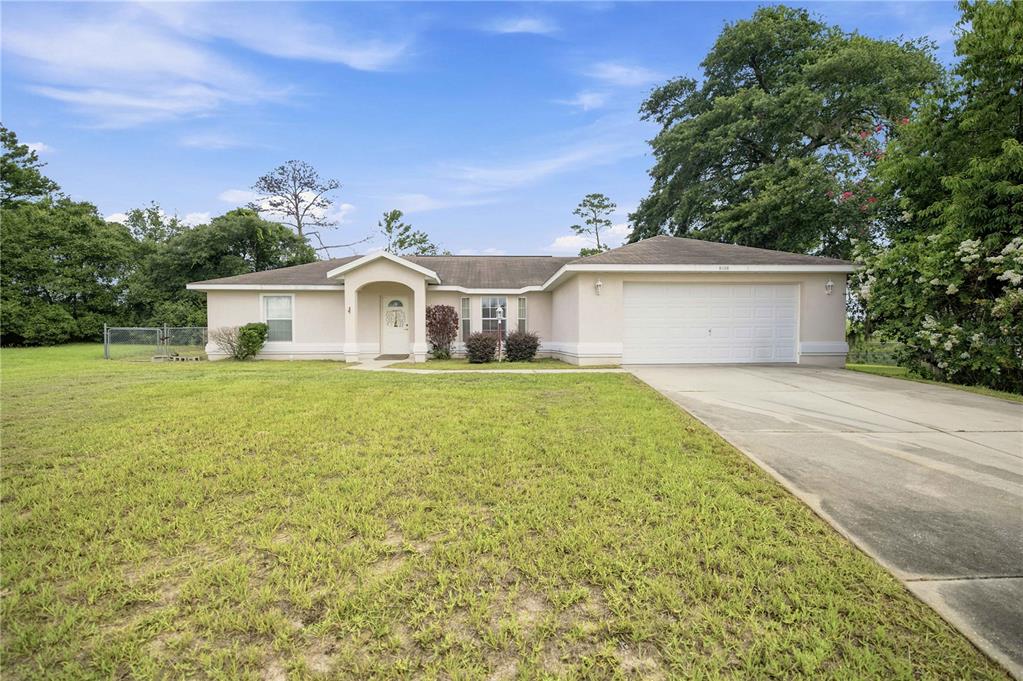 A single-story house with a beige stucco exterior, a two-car garage, and a large lawn — 3377 SW 126TH LANE ROAD, OCALA, FL