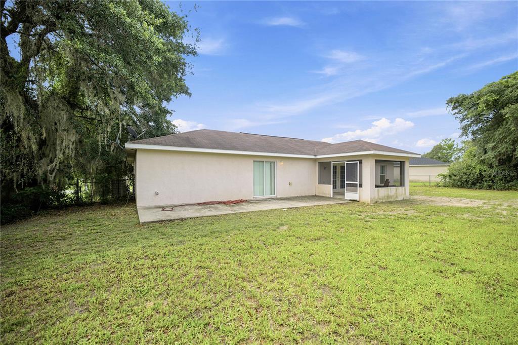 The rear exterior of a single-story house features a concrete patio and a screened porch — 3377 SW 126TH LANE ROAD, OCALA, FL
