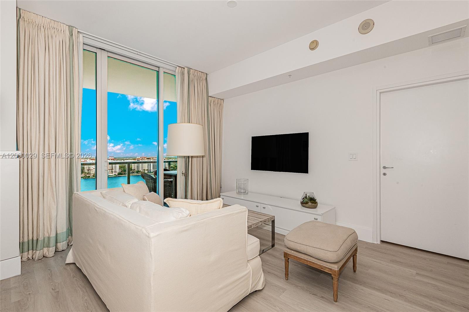 This living room features a white sofa, a wall-mounted television, and floor-to-ceiling balcony windows — 50 S Pointe Dr # 1804, Miami Beach FL 33139, MIAMI BEACH, FL