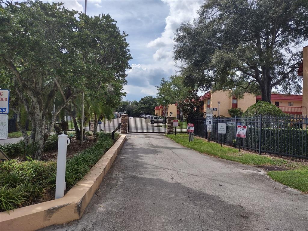 A paved driveway leads to a gated entrance of an apartment complex with mature trees — 2856 N POWERS DRIVE UNIT 114, ORLANDO, FL
