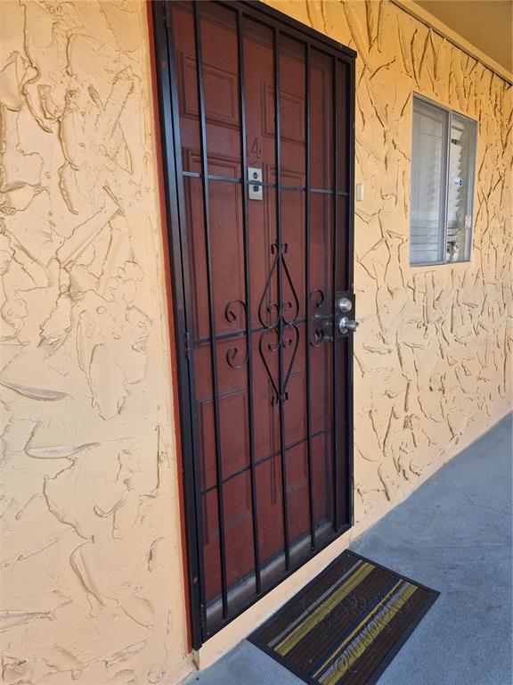 A red door with a black security gate sits on a textured, light-colored exterior wall — 2856 N POWERS DRIVE UNIT 114, ORLANDO, FL