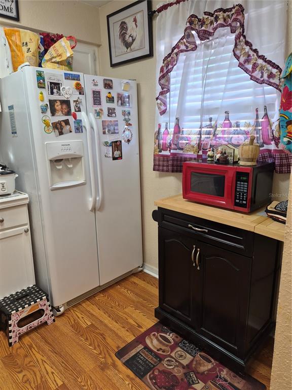 A kitchen features a white refrigerator, a black cabinet with a red microwave, and wood flooring — 2856 N POWERS DRIVE UNIT 114, ORLANDO, FL