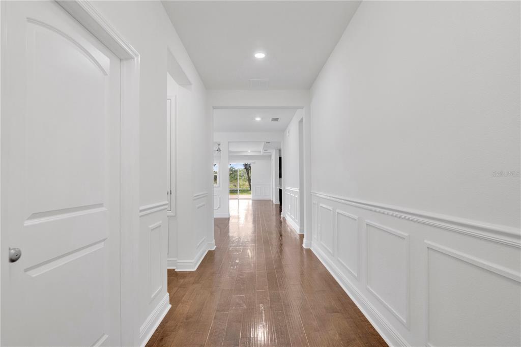 A hallway with white wainscoting and wood flooring leads toward a bright living area — 14254 SERANOA DRIVE, ORLANDO, FL