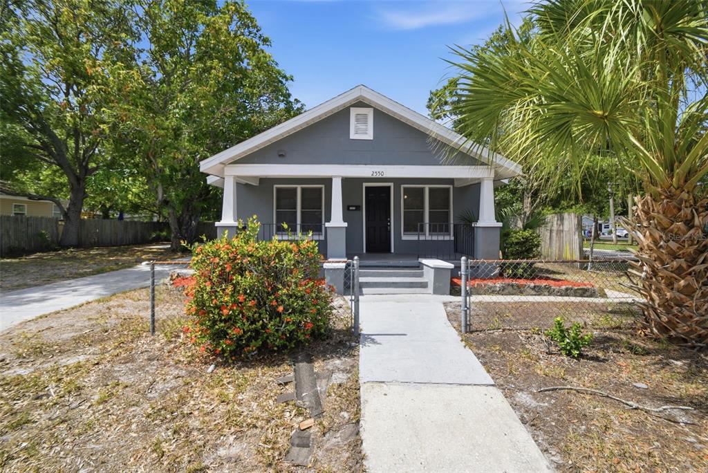 A gray, single-story house features a front porch with white columns and a chain-link fence — 2550 10TH AVENUE S, ST PETERSBURG, FL