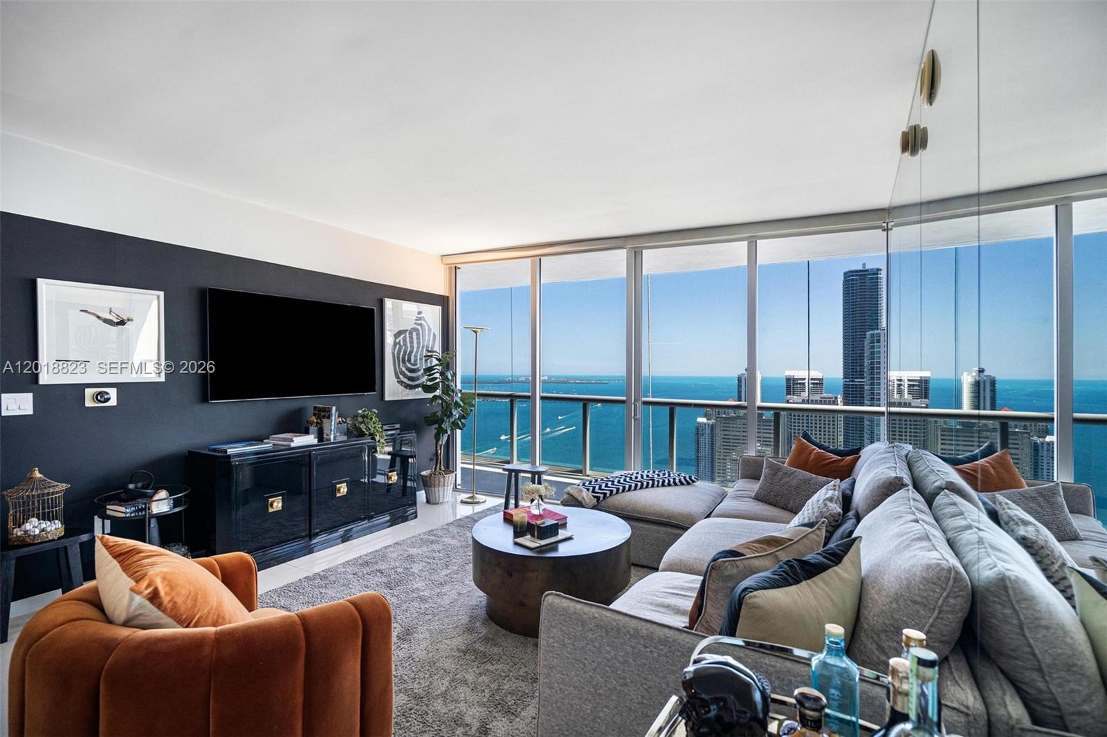 A living room features a dark accent wall, a grey sectional, and floor-to-ceiling ocean views — 495 Brickell Ave # 4911, Miami FL 33131, MIAMI, FL