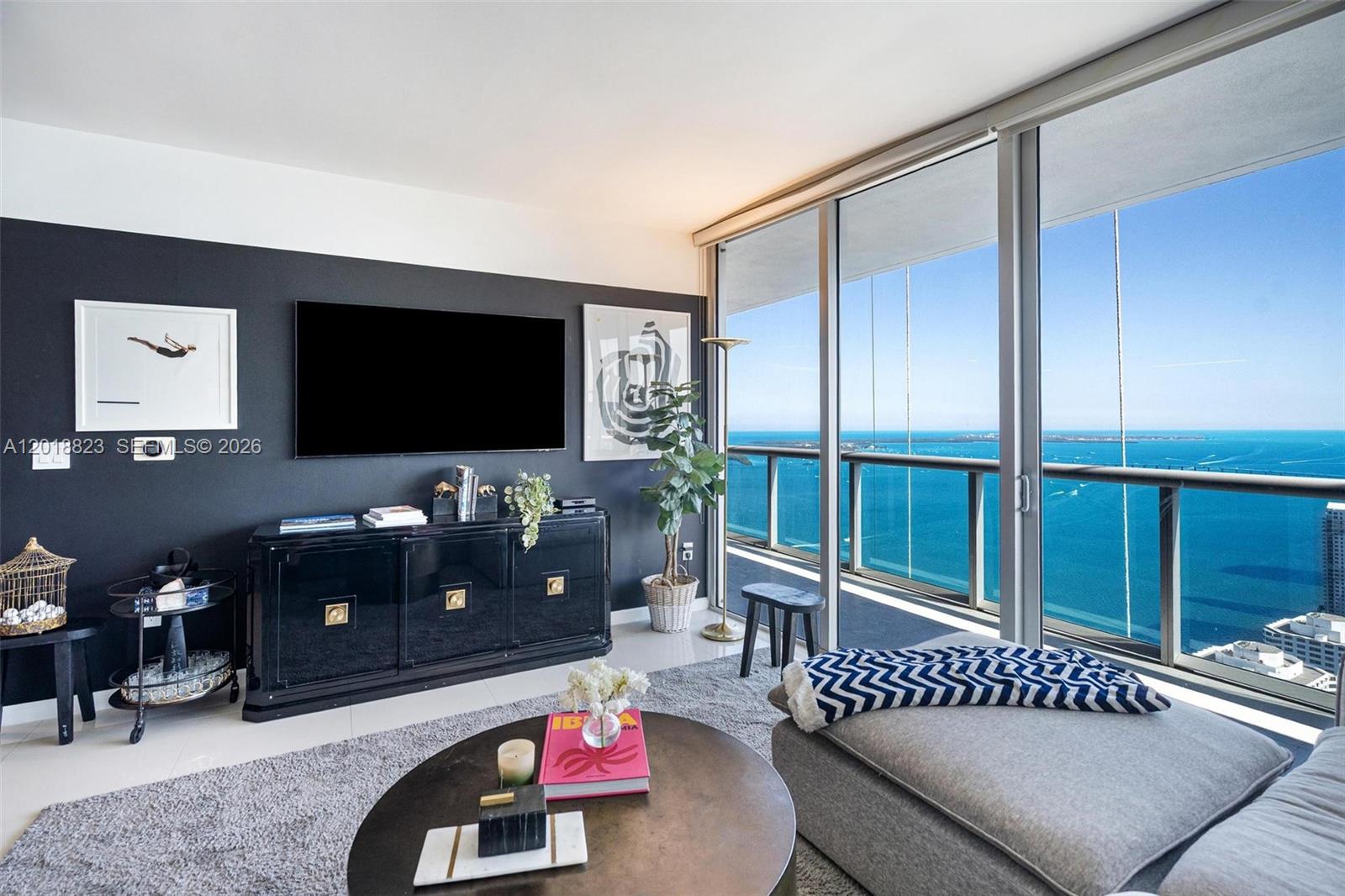 A living room features a black accent wall, a television, and floor-to-ceiling windows overlooking water — 495 Brickell Ave # 4911, Miami FL 33131, MIAMI, FL