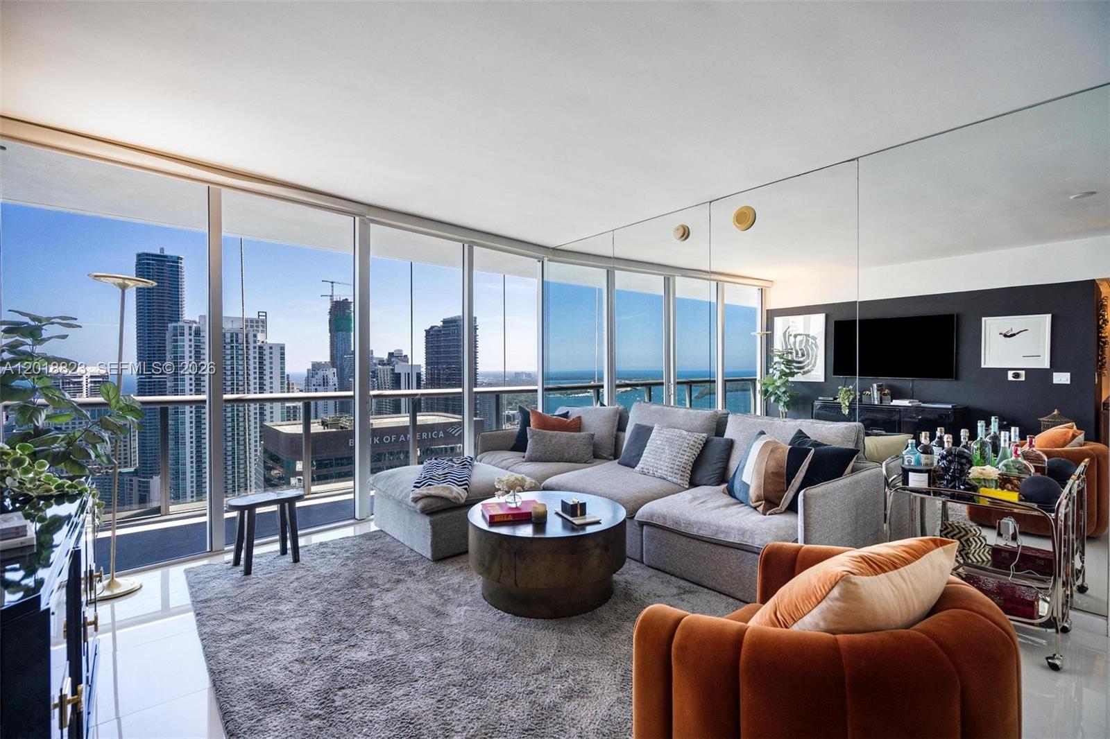 A modern living room features a grey sectional sofa, orange armchair, and floor-to-ceiling windows — 495 Brickell Ave # 4911, Miami FL 33131, MIAMI, FL
