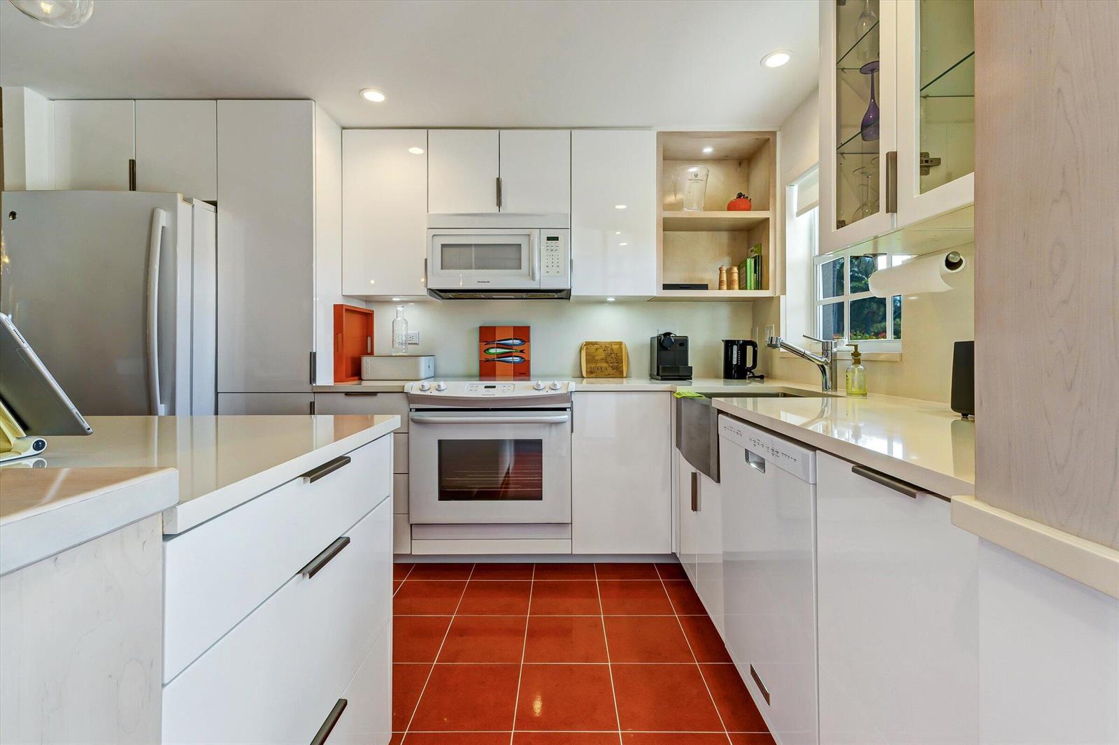 A modern kitchen features white cabinetry, stainless steel appliances, and red tile flooring — 1130 Sugar Sands Boulevard # 189, West Palm Beach FL 33404, WEST PALM BEACH, FL