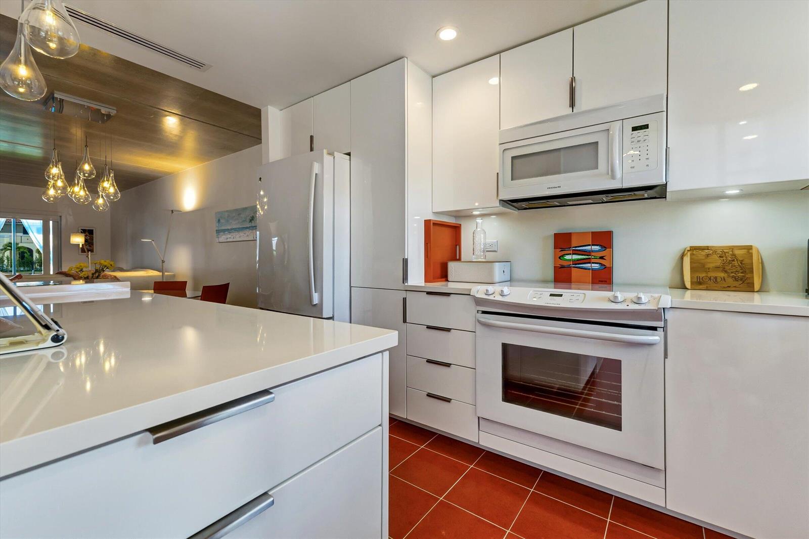 A modern white kitchen features a quartz island, stainless steel appliances, and red tile flooring — 1130 Sugar Sands Boulevard # 189, West Palm Beach FL 33404, WEST PALM BEACH, FL