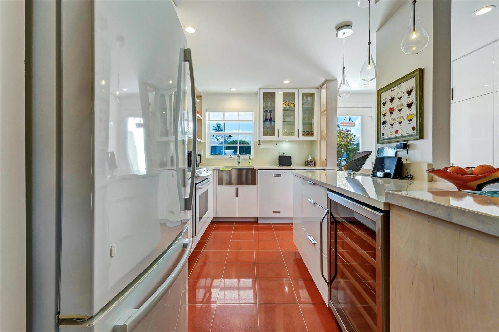 A modern kitchen features white cabinetry, stainless steel appliances, and glossy red tile flooring — 1130 Sugar Sands Boulevard # 189, West Palm Beach FL 33404, WEST PALM BEACH, FL
