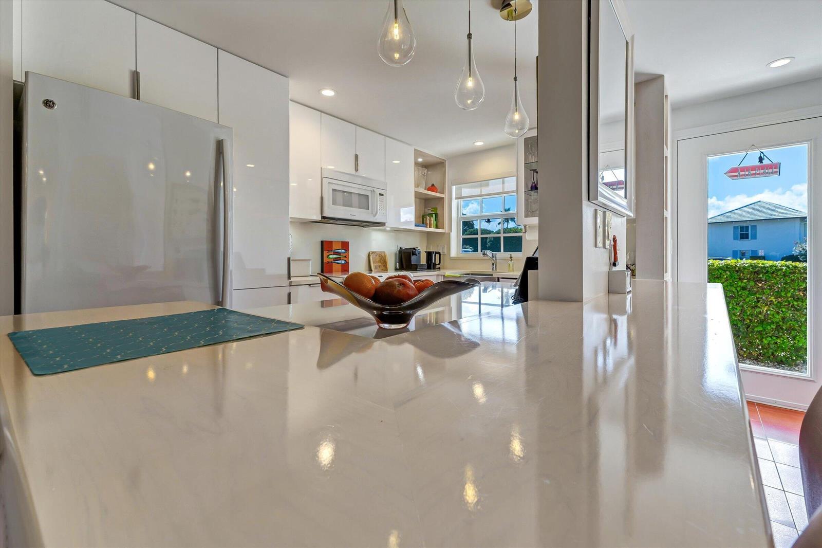 A modern kitchen features white cabinetry, a light countertop, and a view of the outdoors — 1130 Sugar Sands Boulevard # 189, West Palm Beach FL 33404, WEST PALM BEACH, FL